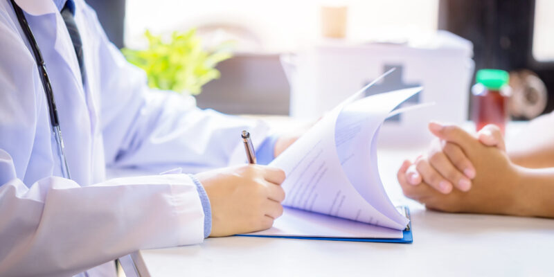 Doctor man consulting patient while filling up an application form at the desk in hospital. Medicine and health care concept