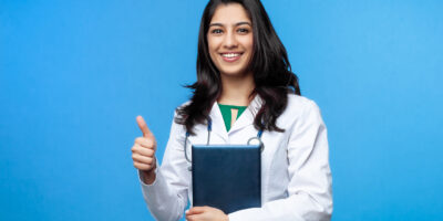 Beautiful young Asian girl doctor, with a laptop for records isolated on a blue background. Medical student general practitioner. The concept of medical education in India
