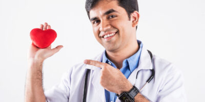 Handsome Indian Male Doctor holding red stuffed heart toy as a heart care concept. standing isolated over blue background