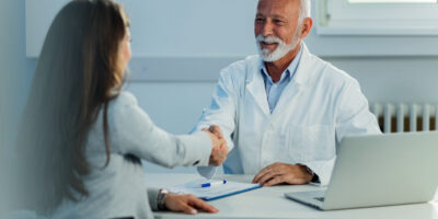 Happy mature doctor and his female patient shaking hands after medical appointment at clinic.